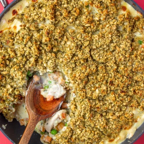 Chicken pot pie with a stuffing crust in large pan with a wooden spoon on a red background.