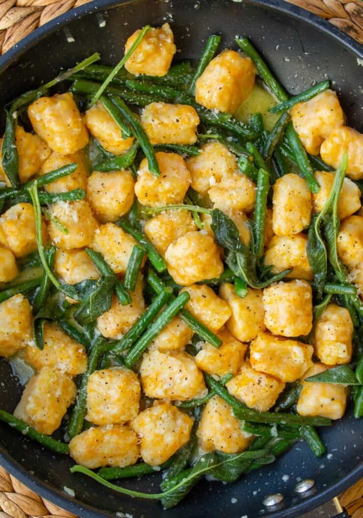 Overhead shot of butternut squash gnocchi in large pan scattered with green beans