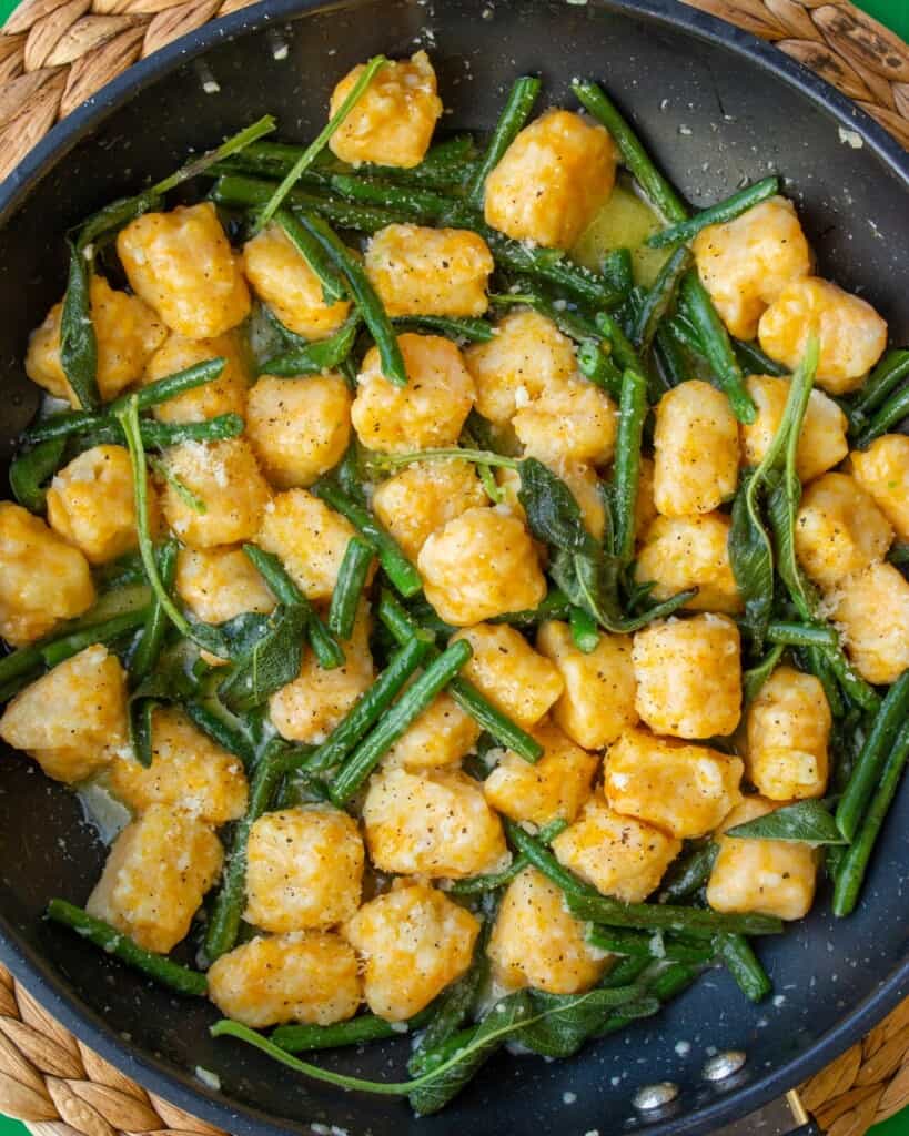 Overhead shot of butternut squash gnocchi in large pan scattered with green beans