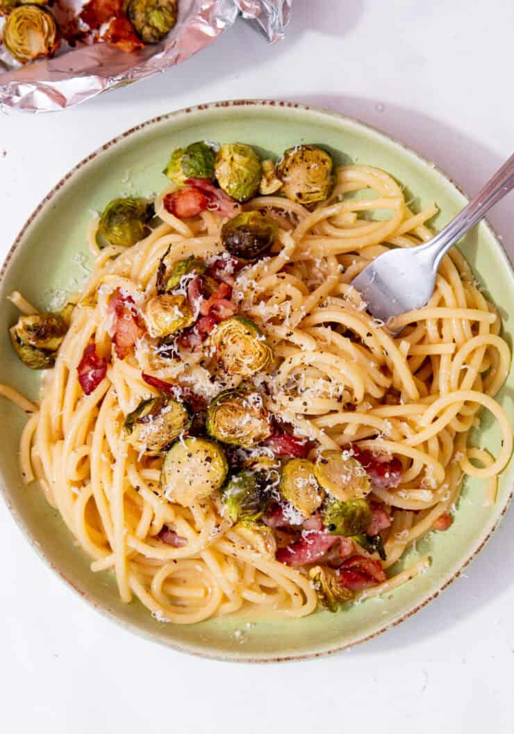 Spaghetti with roasted brussel sprouts and bacon in a bowl with a spoon.