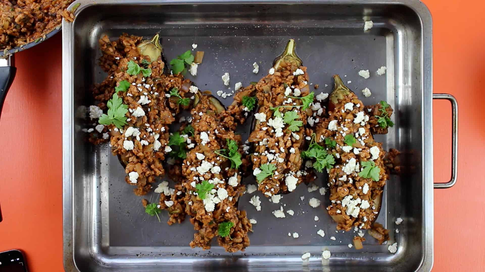 Aubergines filled with mince and garnish on baking tray with feta and parsley