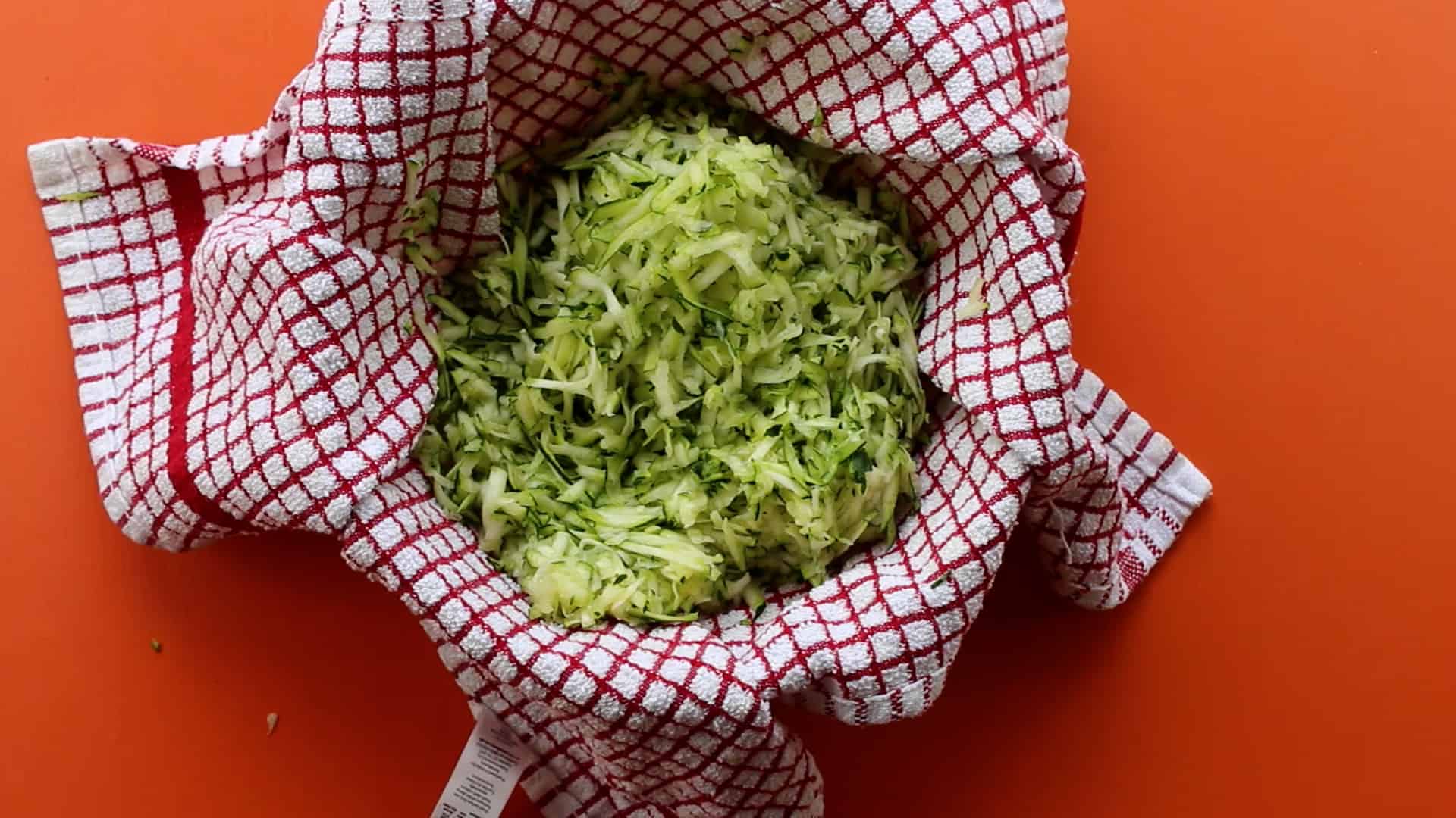 Grated courgette on tea towel in a bowl on an orange background.