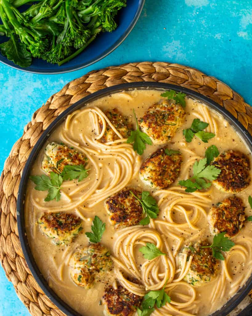 Swedish Gravy Spaghetti with Pork and Courgette Meatballs topped with parsley in a large pan on a straw mat next to a bowl of broccoli.