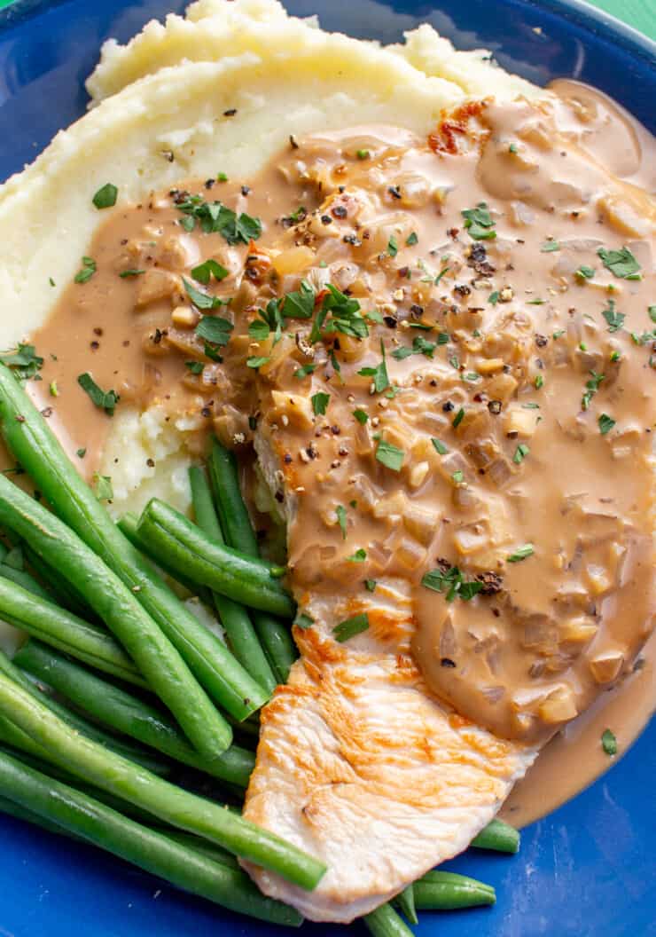 Turkey Steaks with Creamy Peppercorn Sauce and Mash and green beans in a blue bowl.
