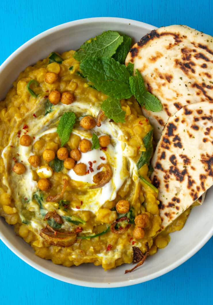 Yellow Split Pea Dhal with Crispy Chickpeas topped with fresh mint and a swirl of yogurt and 2 pieces on naan bread in a white bowl.