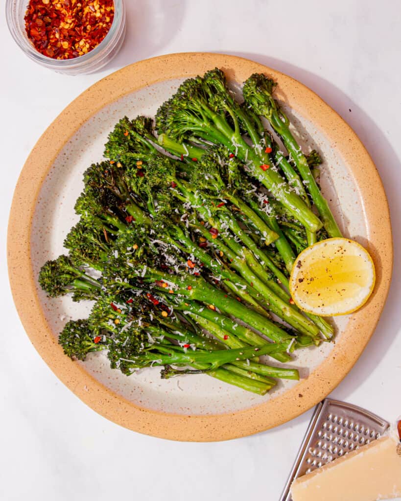 Lots of tenderstem broccoli displayed on a plate with a wredge of lemon.