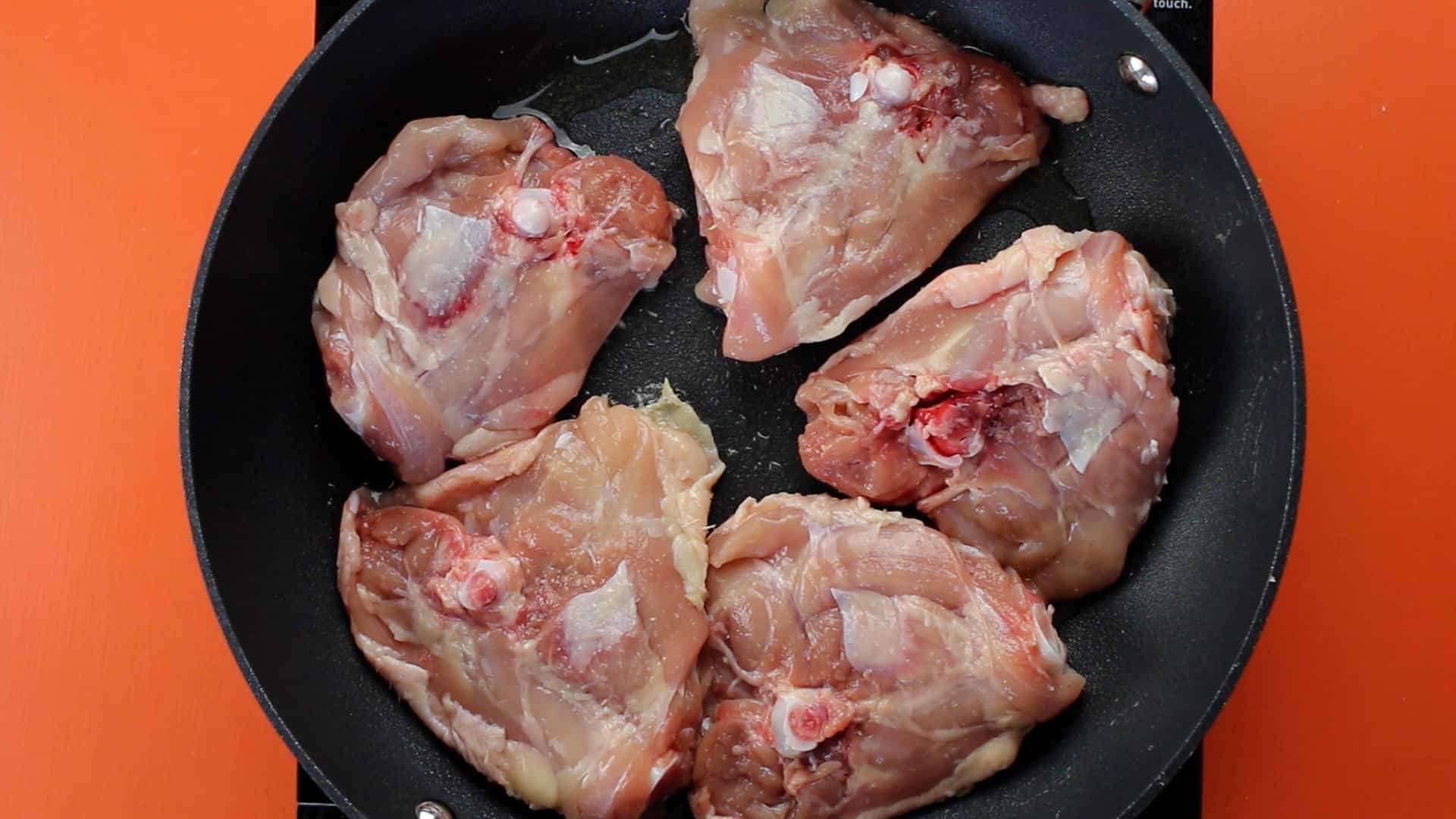 Chicken thighs skin side dow in frying pan on stove