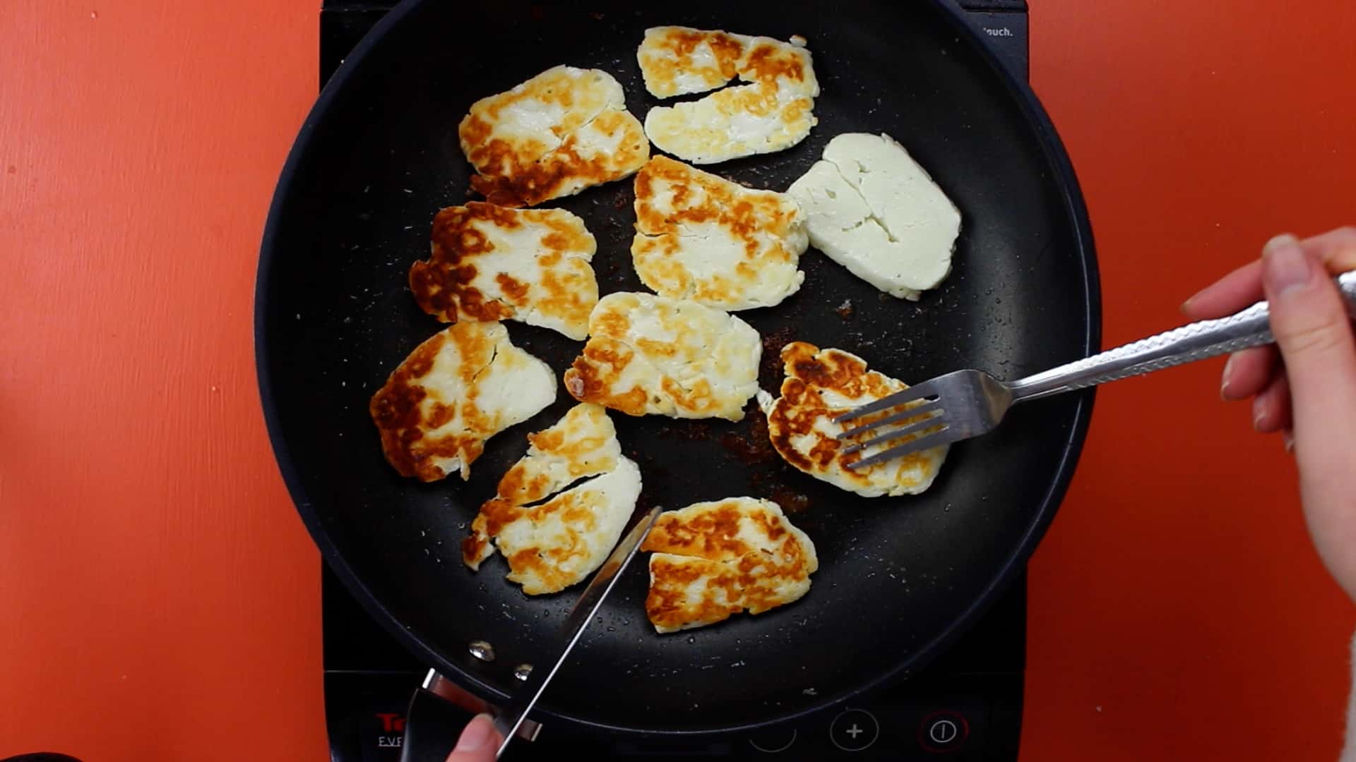 Halloumi slices browned in frying pan with with fork and knife used to rotate the slices..