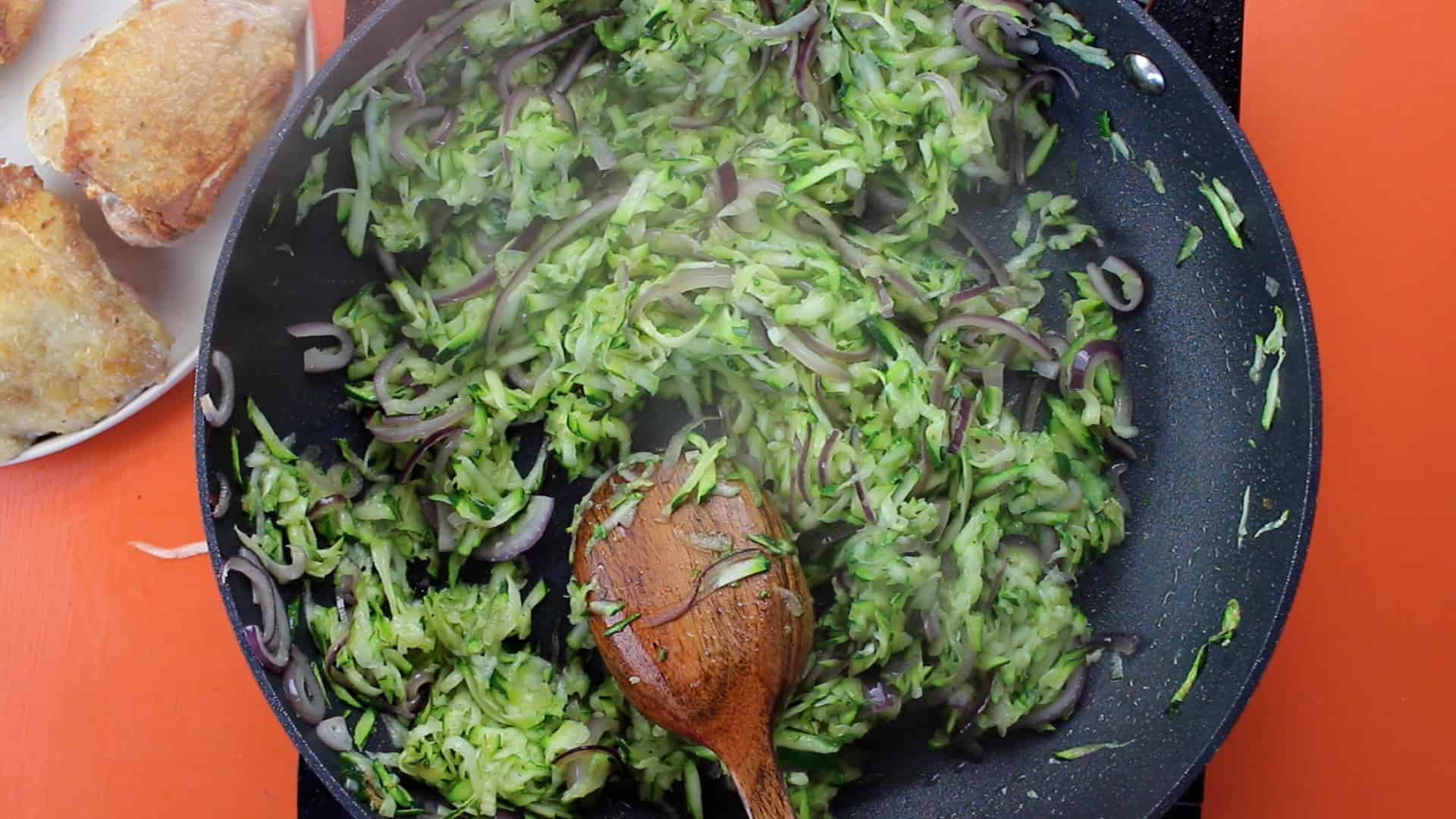 Grated courgettes added to the pan with the fried red onion and mixed with a wooden spoon.