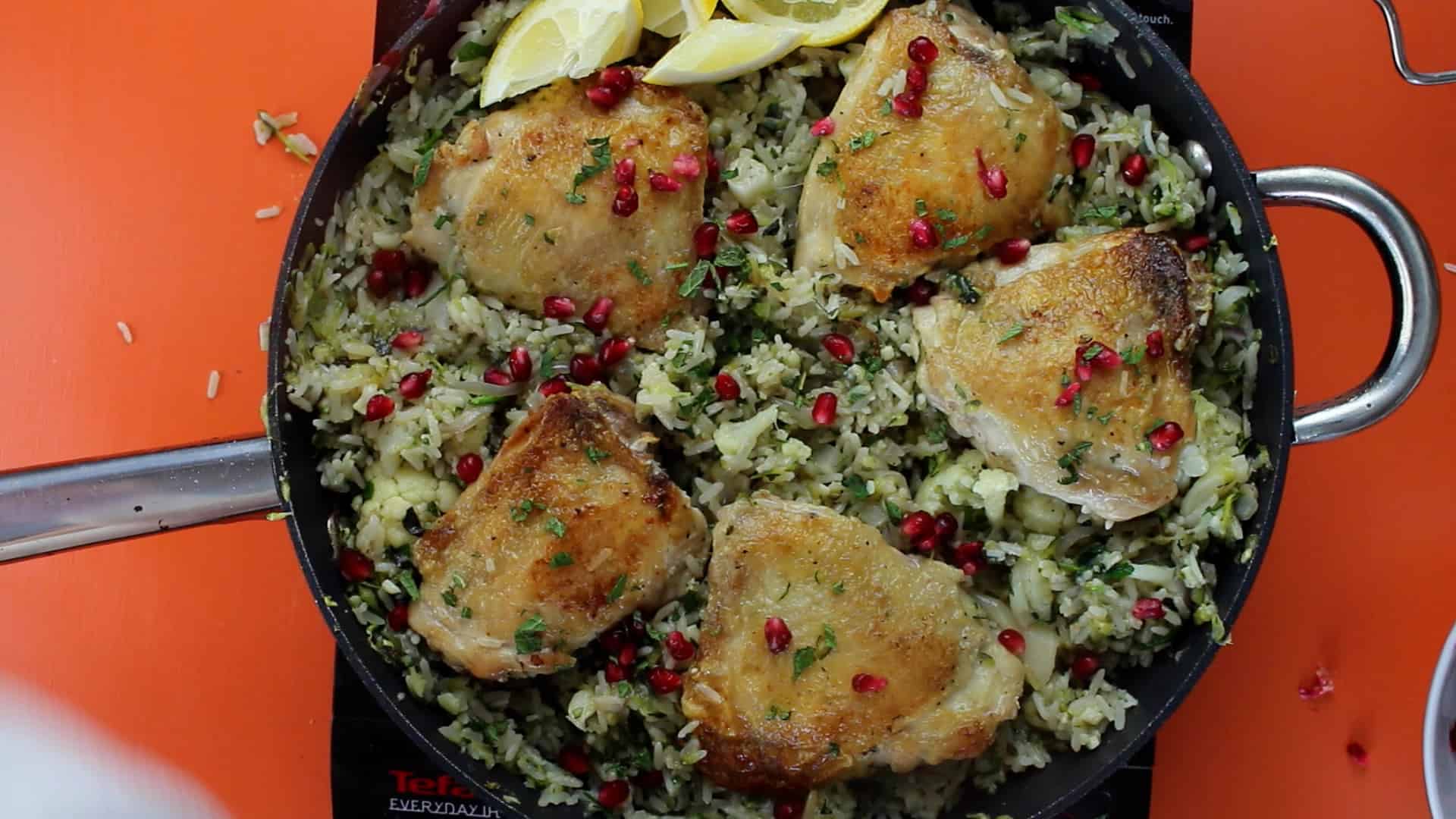 Lebanese Inspired Chicken Pilaf ready in pan garnished with lemon wedges and pomegranate seeds.