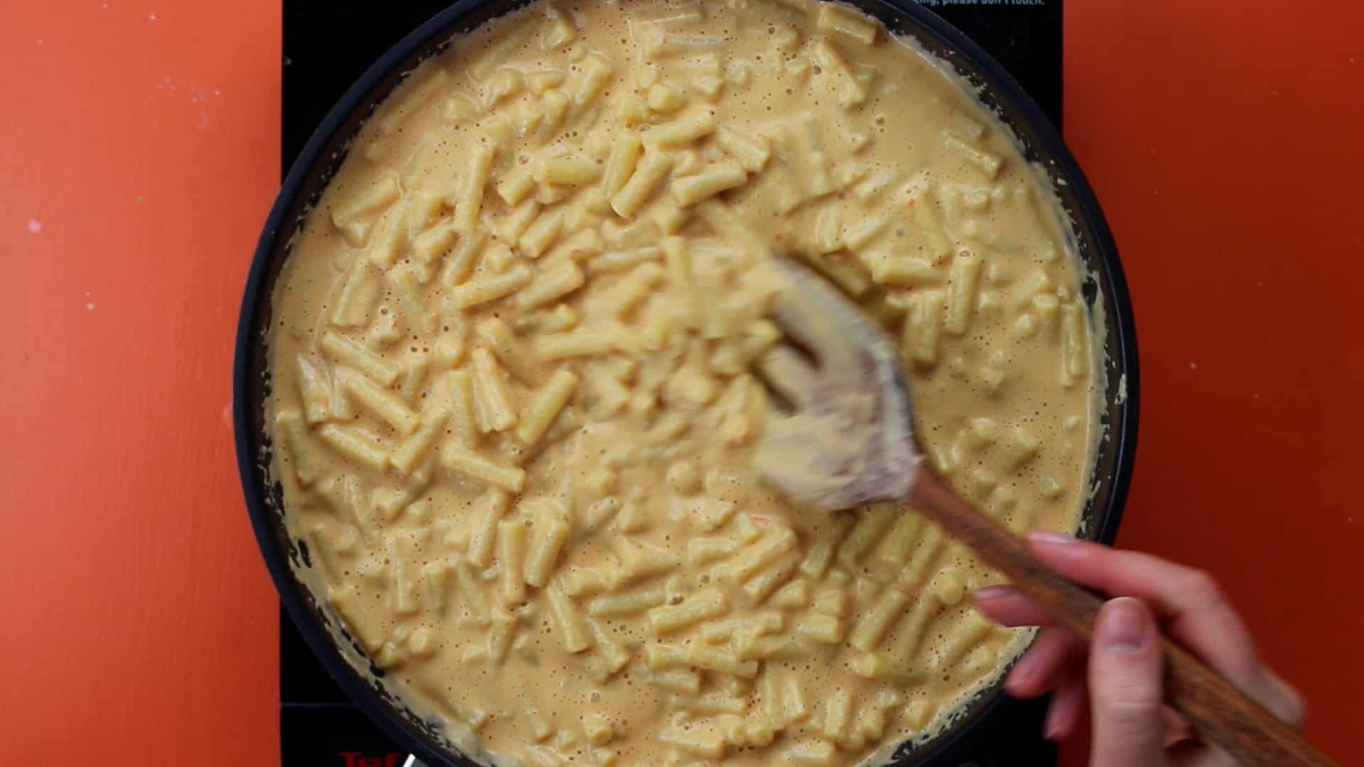Macaroni pasta ready in pan and being stirred with wooden spoon