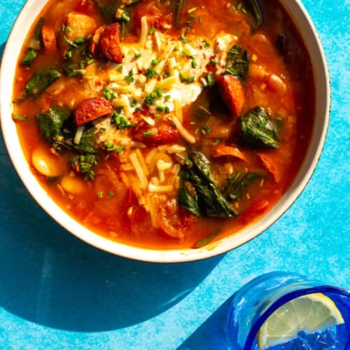 Slow Cooker Chorizo & Butter Bean Soup in a bowl with wilted spinach, chorizo cubes, butter beans topped with cheese and sour cream.