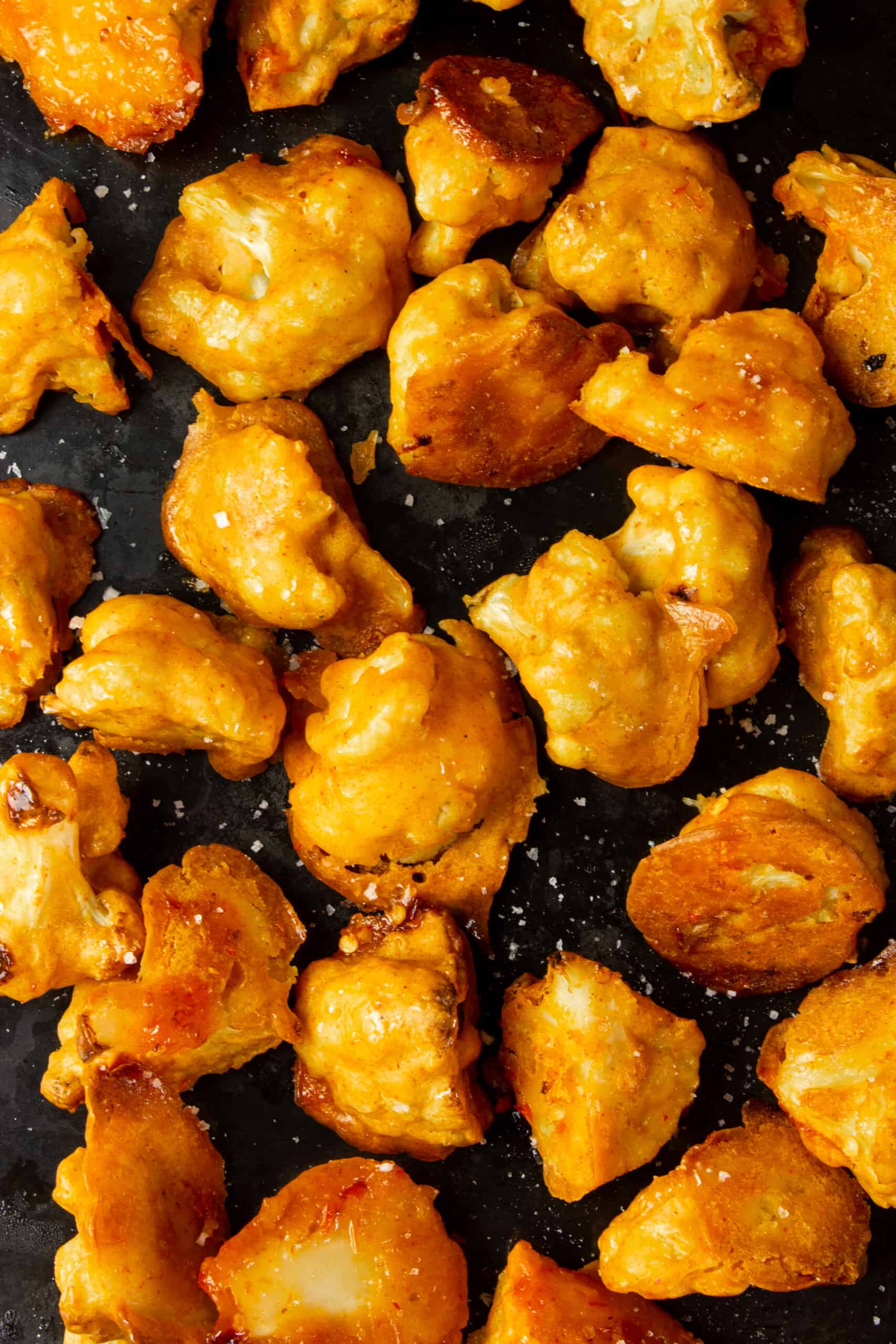 Golden browned cauliflower bites on a black baking tray. 