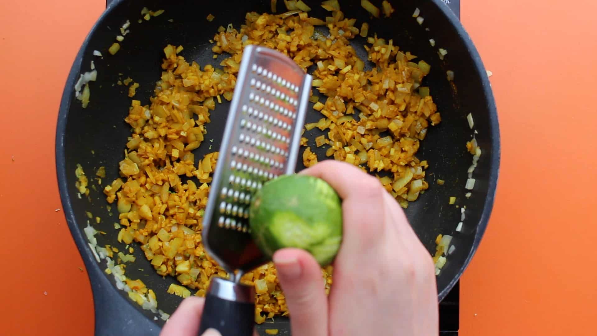 Lime being grated into pan over onions