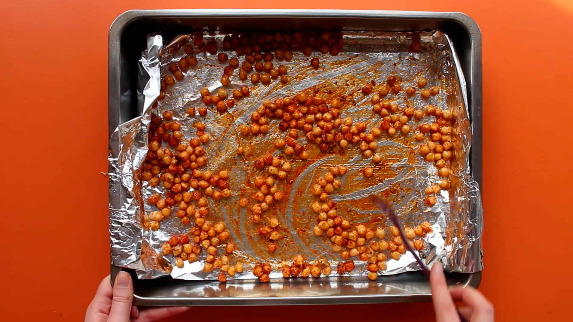 Chick peas scatter over a baking tray and being mixed together with spices