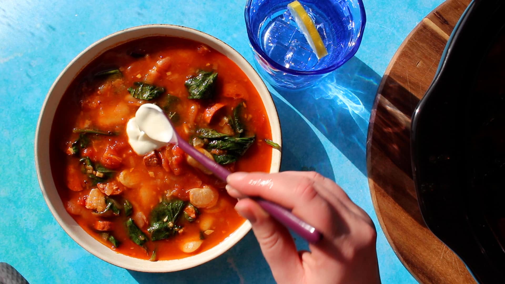 A bowl of Spanish Chorizo and Butter Bean Slow Cooker Stew with a dollop of sour cream and a blue glass with water.