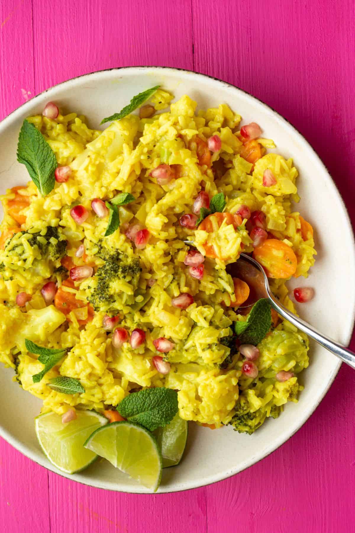 Close up of yellow rice with fresh mint, vegetables, pomegranate and lime wedges.