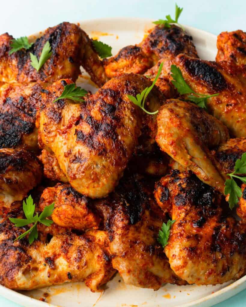 Charred and browned chicken wings on a plate garnished with parsley.