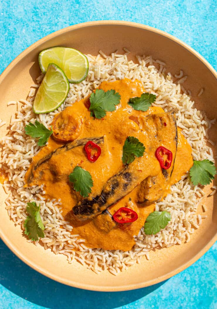Aubergine Penang Curry in a bowl on a bed of rice, garnished with a wedge of lime and coriander.