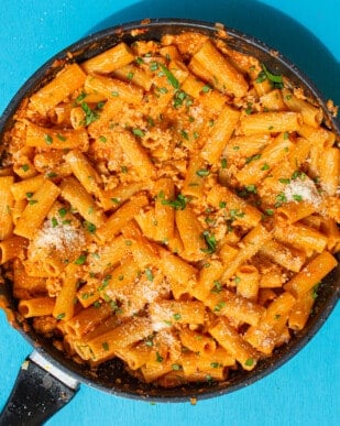 Spicy Vodka rigatoni topped with fresh chopped basil and grated parmesan in a large pan on a bright blue background.