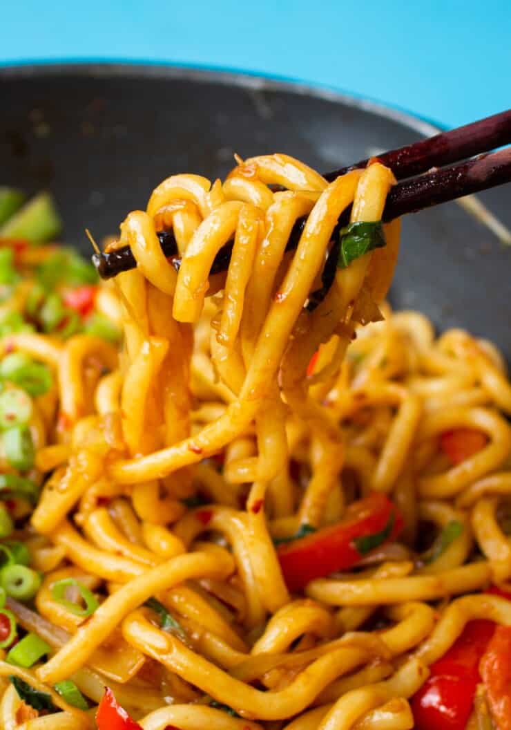 Close up of Chilli oil udon noodles with red peppers and spring onions with chopsticks used to lift the udon noodles from the pan.