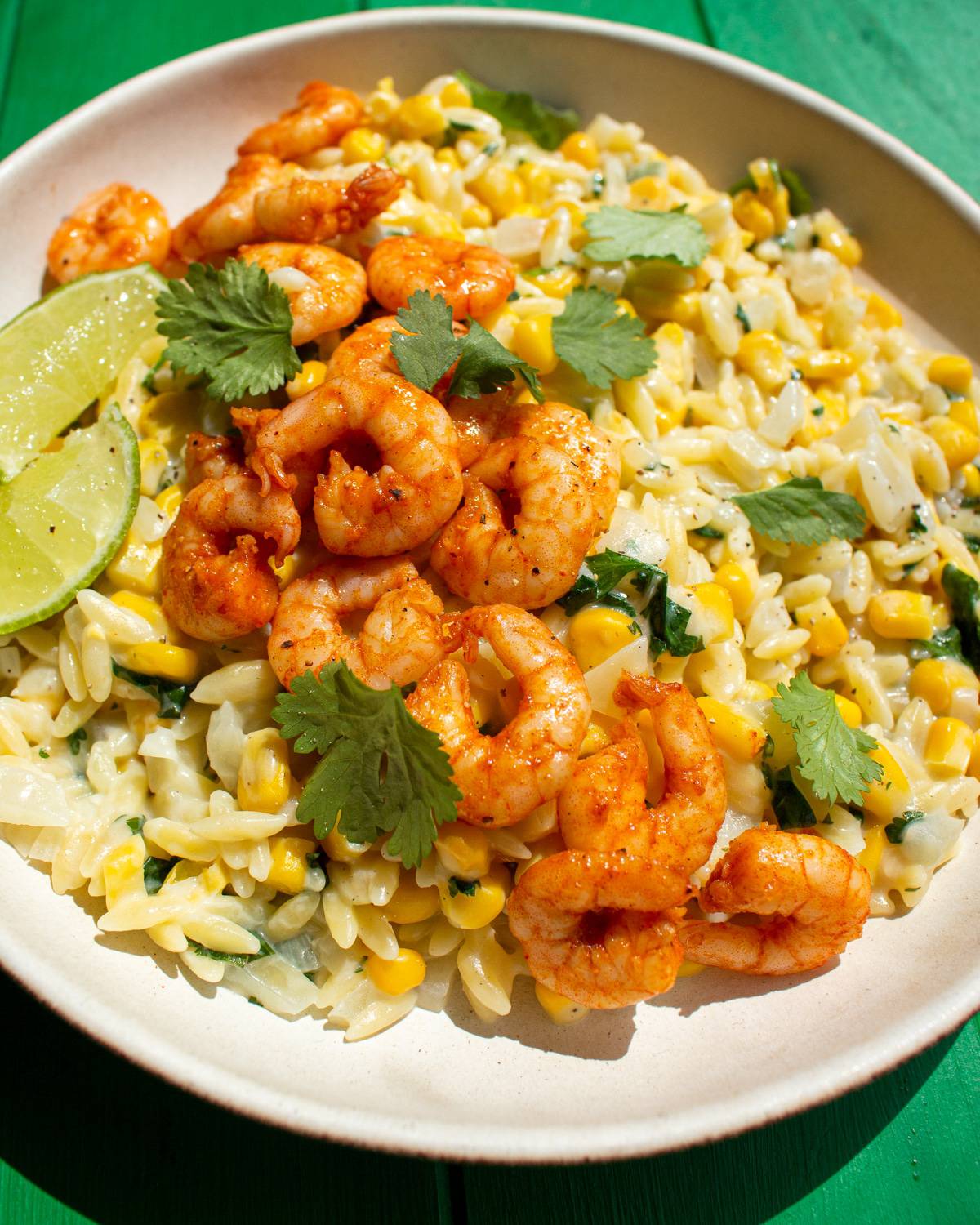 Sweetcorn and orzo topped with paprika covered prawns. Garnished with lime wedges and parsley.