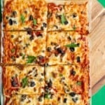 Sheet Pan Puttanesca Pizza with mozzarella, black olives, capers and fresh parsley cut into 8 pieces on parchment paper on a wooden board.