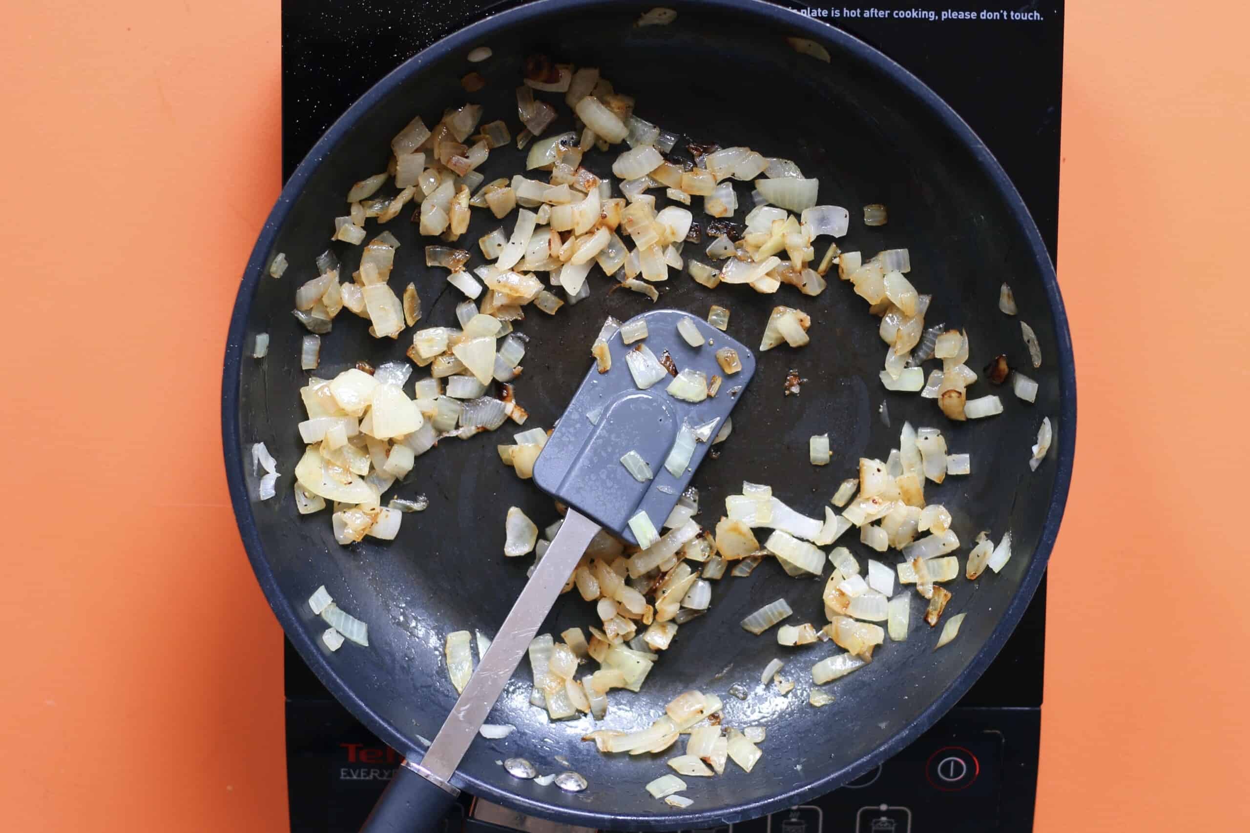 Onions sautéing in frying pan on stove with spatula