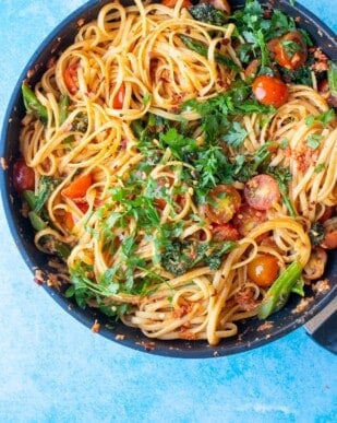 Spicy Crab Linguine in a pan with cherry tomatoes and topped with fresh chopped parsley on a blue background.