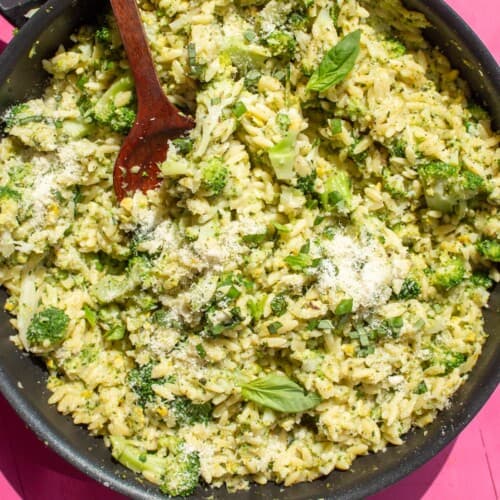 Broccoli Pesto Orzo in large pan with a wooden spoon with grated parmesan and basil topping.