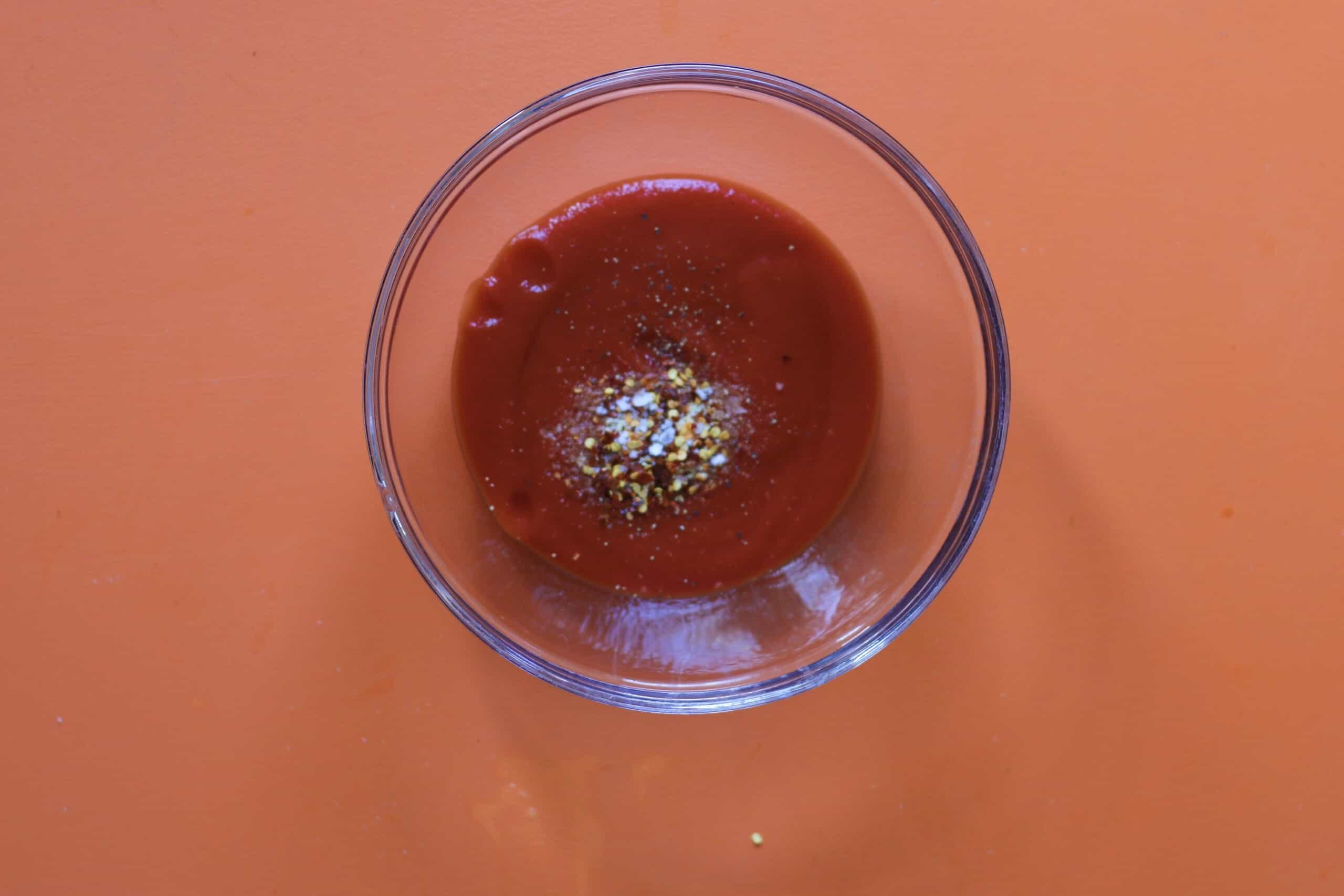 Passata with herbs and seasoning in a glass bowl on an orange background.