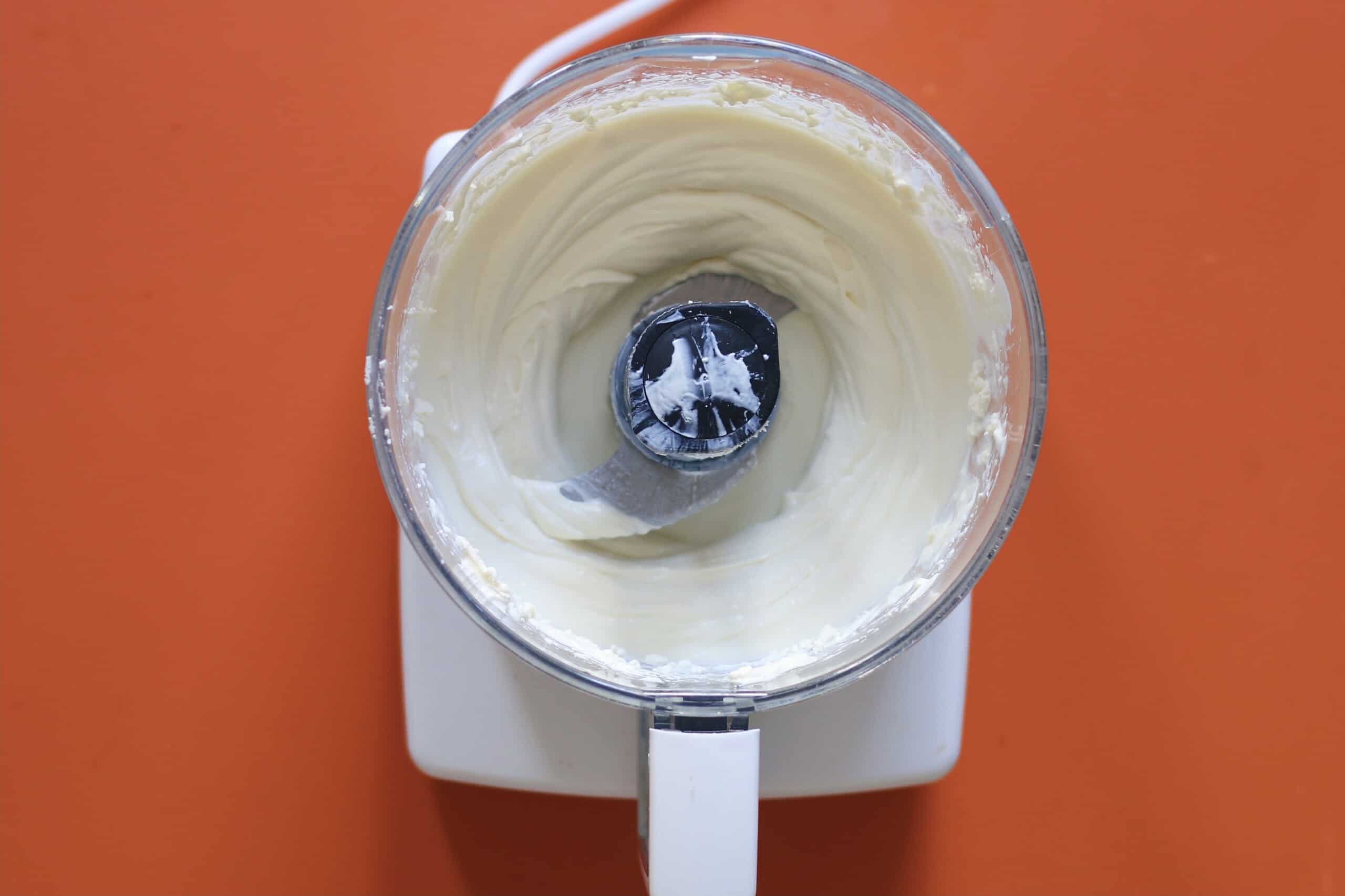 Whipped feta blended together in a food processor on an orange background.