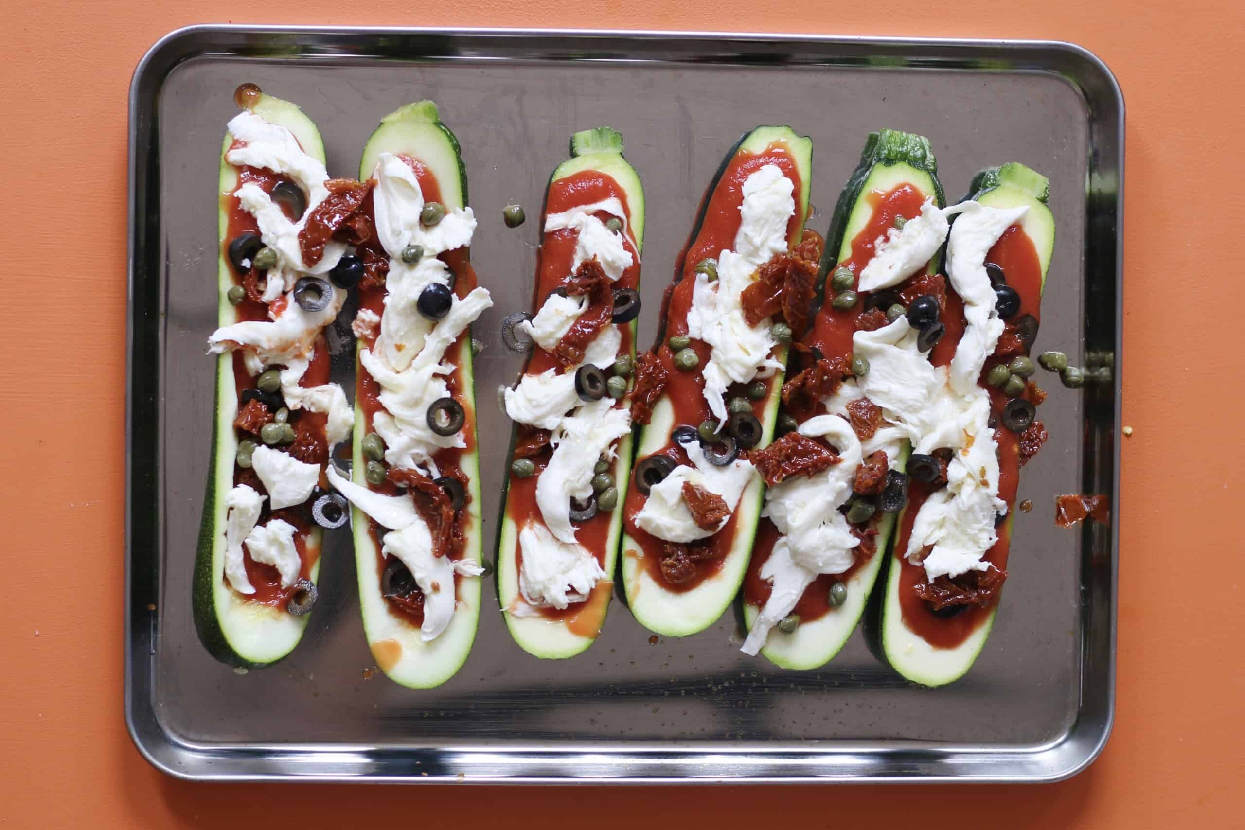 Courgette boats with mozzarella, olives and pasta filling on baking tray