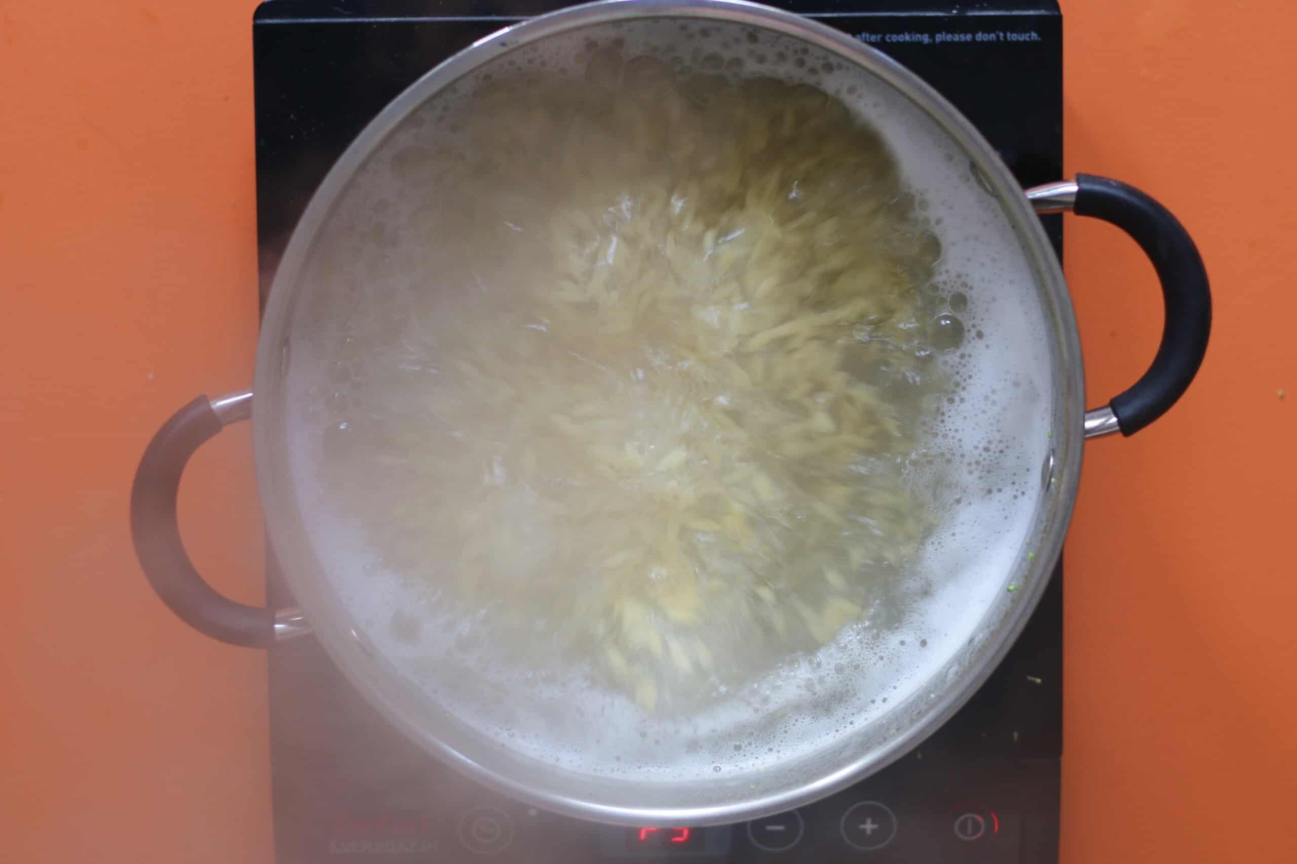 Orzo in saucepan with boiling water on cooker