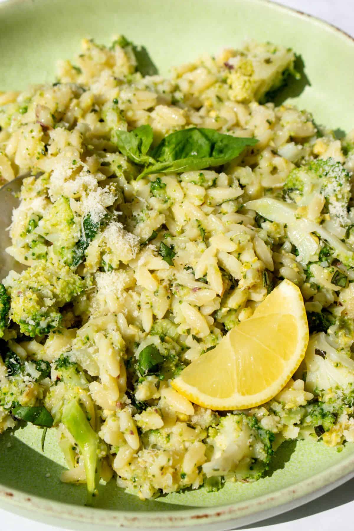 Close up with pieces of broccoli, pesto and orzo in a bowl with a lemon wedge.