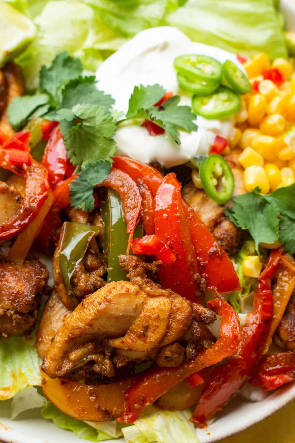 Close up shot of chicken fajita ingredients with salad topped with sweet corn, sour cream and green chillies.