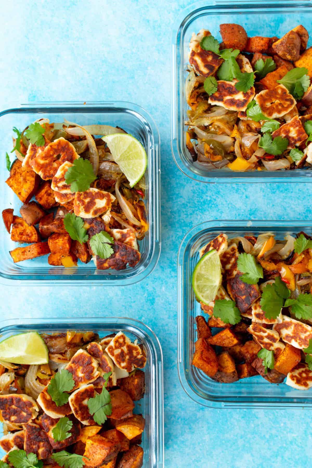 Halloumi and sweet potatoes in 4 square glass meal prep containers topped with coriander and a lime wedge on a blue background.