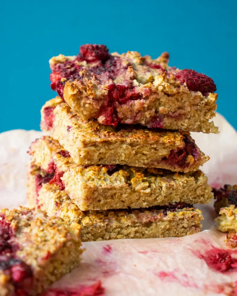 4 pieces of raspberry oat bakes piled on top of each other on parchment paper with a blue background.