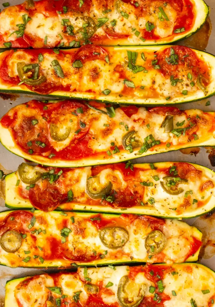 Overhead shot of courgette halves roasted on baking tray with cheesy, pepperoni topping
