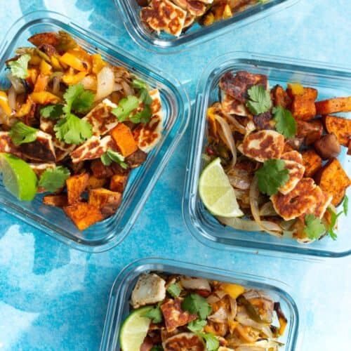 4 square glass meal prep containers filled with sweet potato cubes, peppers, topped with golden browned halloumi, coriander and lime wedges.