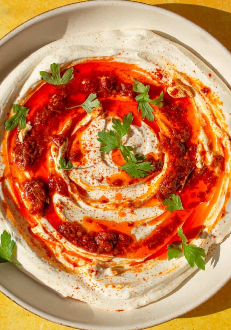 Whipped Feta dip topped with Harissa and fresh parsley in a bowl on a yellow background.