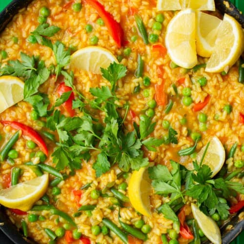 Vegetarian Paella in a large pan topped with fresh parsley and lemon wedges.