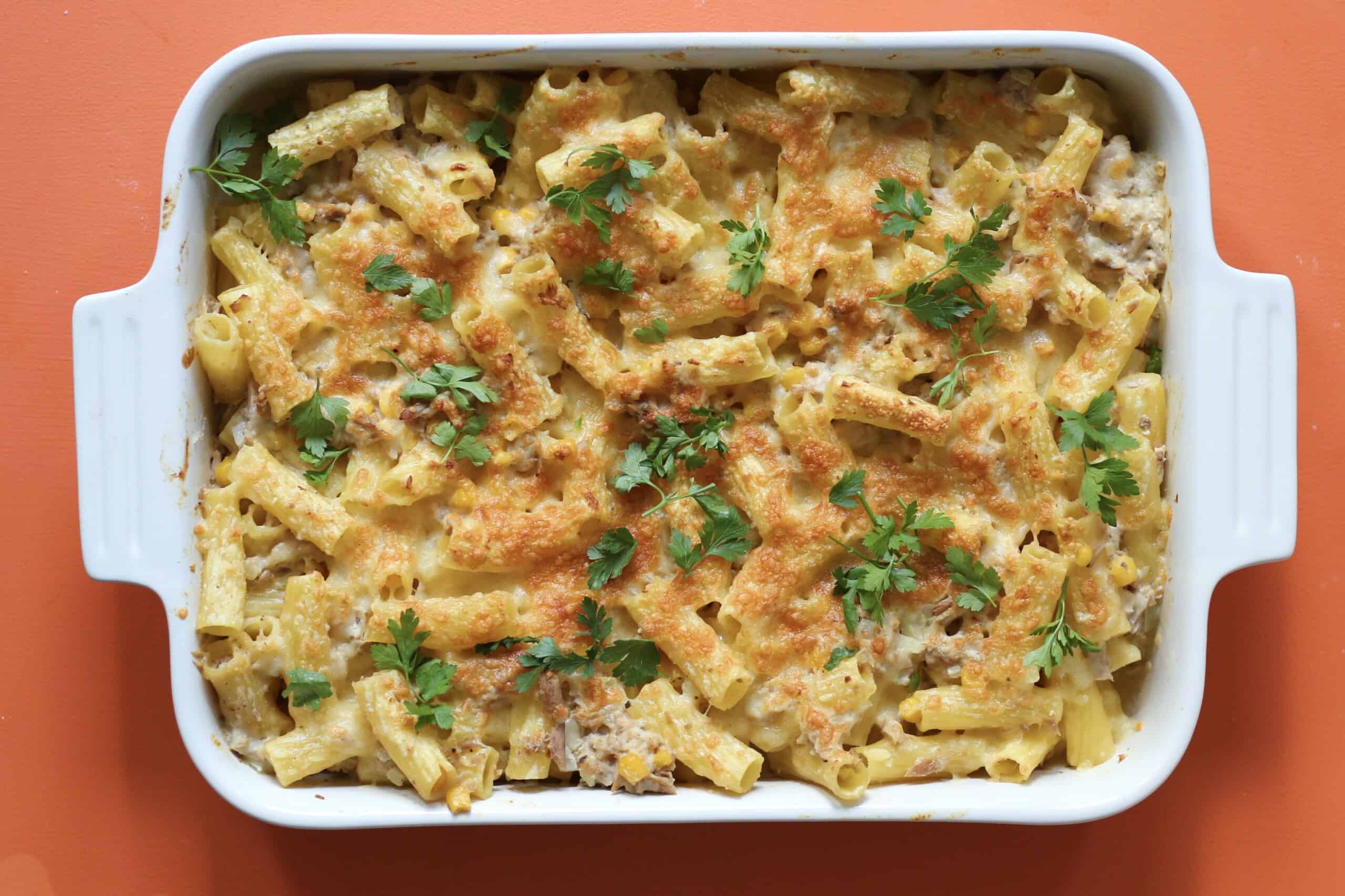 Tuna bake bake browned in the oven in a rectangular white dish topped with fresh parsley on an orange background.