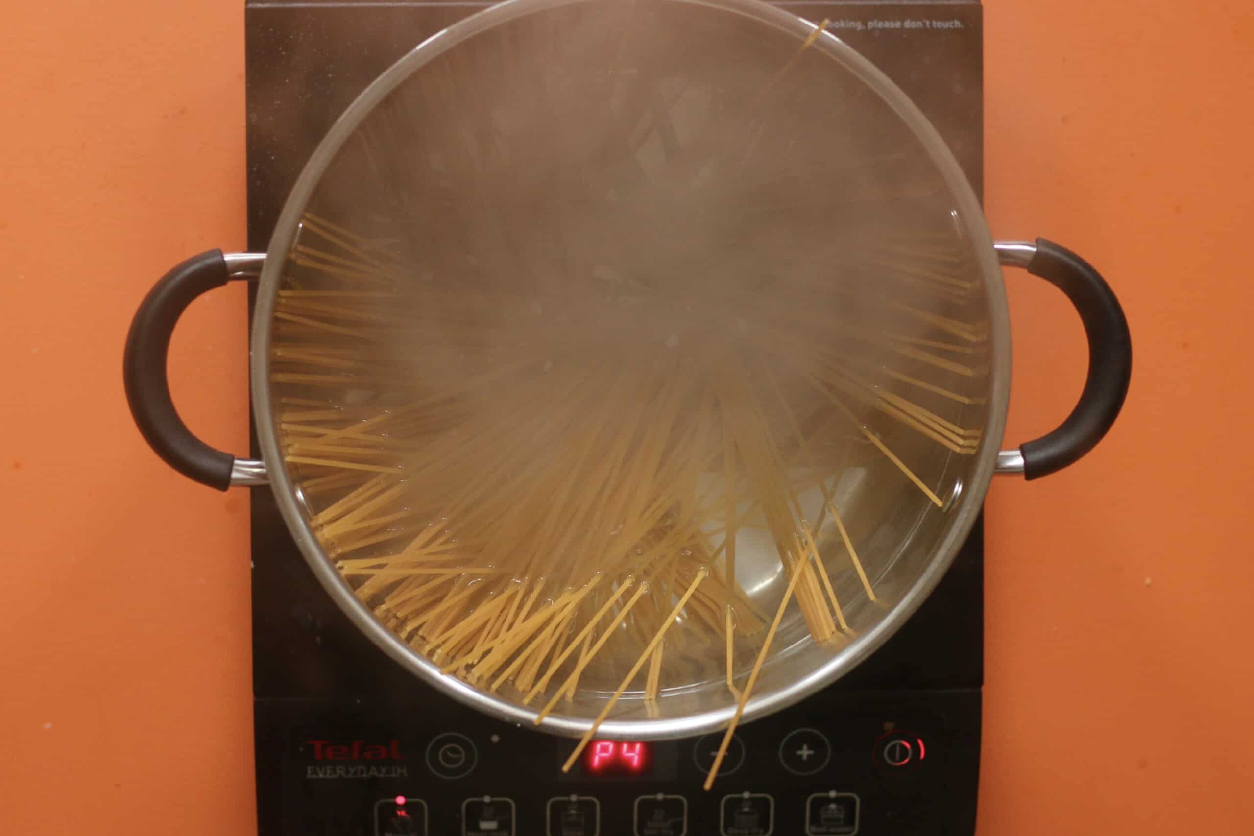 Dry spaghetti in  boiling water in a large saucepan on a stove on an orange background.