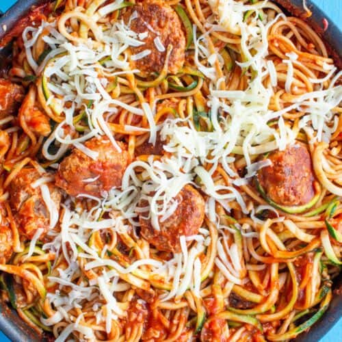 Meatballs in spaghetti with tomato sauce topped with mozzarella in a large pan on a blue background.
