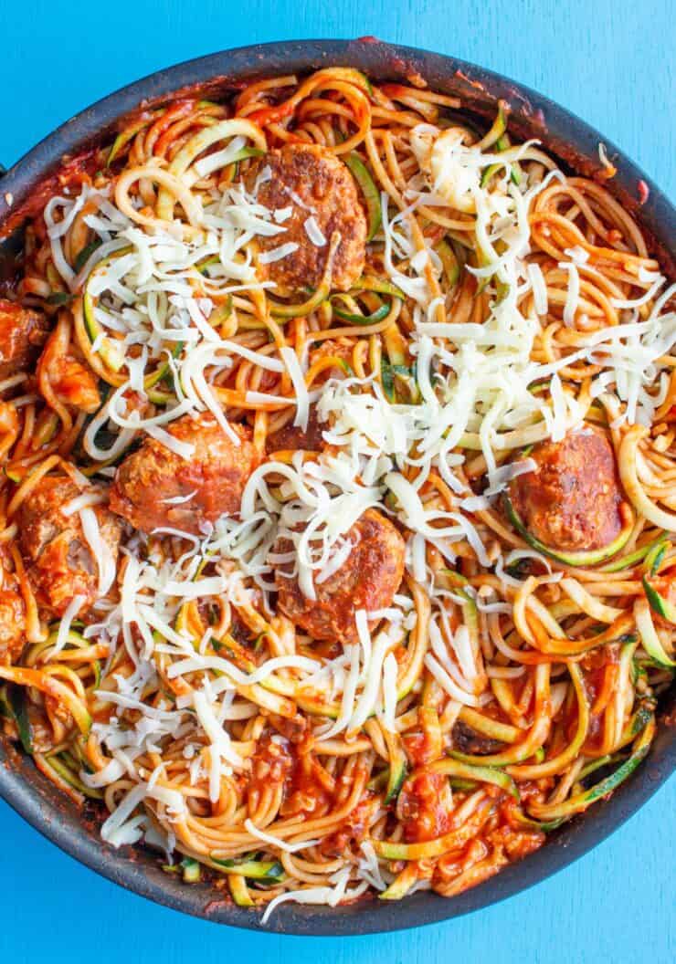 Meatballs in spaghetti with tomato sauce topped with mozzarella in a large pan on a blue background.