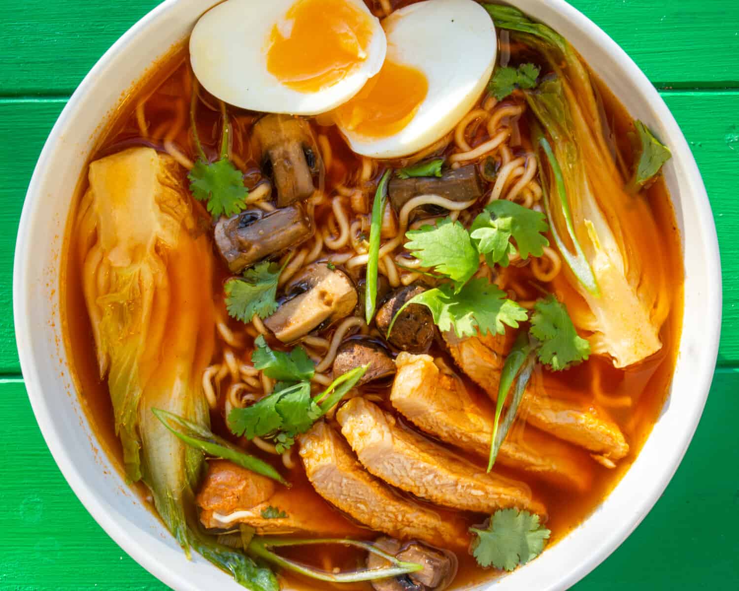 ramen bowl with sliced pork, boiled egg sliced in half and coriander to top