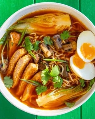 ramen bowl with sliced pork, boiled egg sliced in half and coriander to top