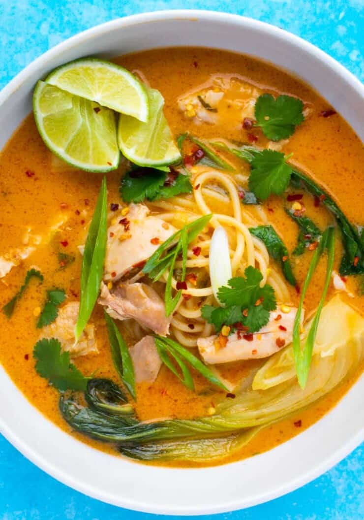 thai soup with noodles and chicken. Garnished with coriander, spring onion and lime wedges