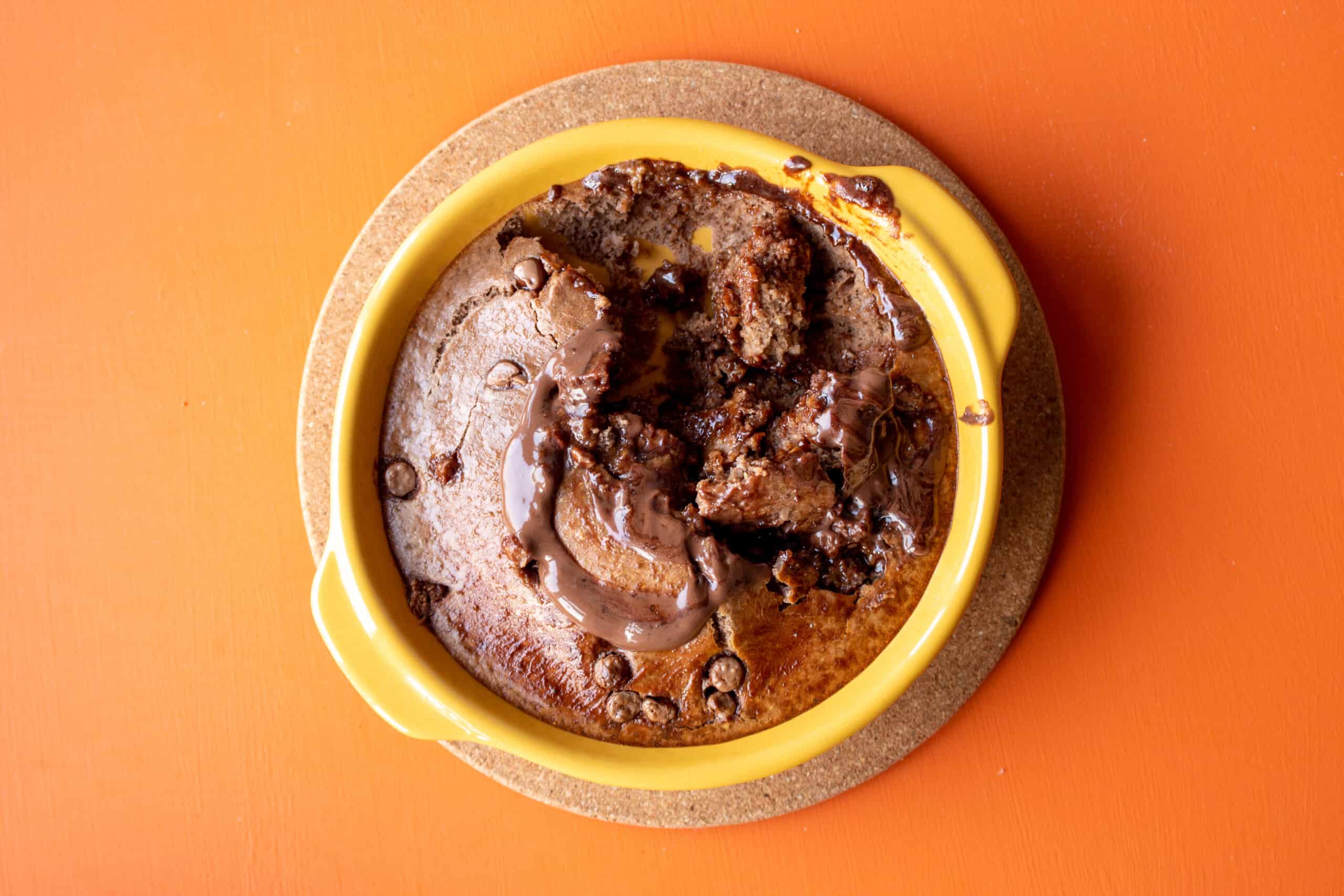 Nutella baked oats with a spoon full from the middle eaten on a heat mat on an orange background.